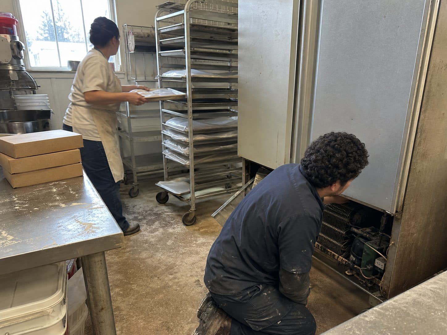 Technician kneeling to repair the compressor of a bakery reach-in refrigerator