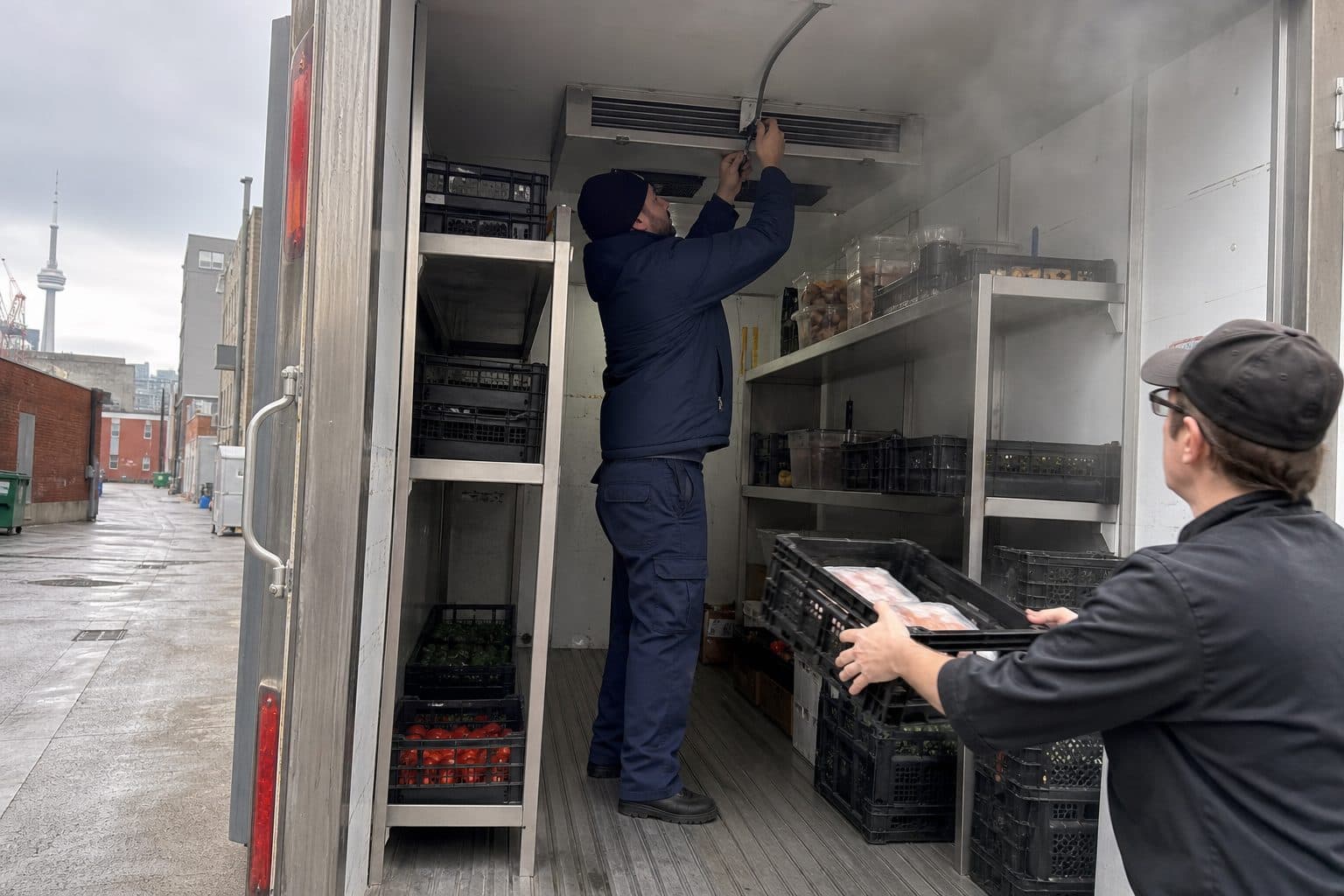 Technicians fitting shelving and placing a temperature probe inside a refrigerated trailer